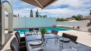 Un área de comedor al aire libre con piscina, mobiliario de mimbre y vistas despejadas del vecindario.