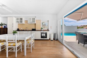 Cocina moderna con armarios blancos, horno empotrado y comedor con sillas blancas y cojines amarillos.