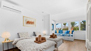 Habitación de hotel con dos camas, ventana con vistas, aire acondicionado de pared y un cuadro enmarcado.