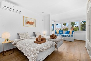 A hotel room with two beds, a window with a view, a wall-mounted air conditioner, and a framed picture.