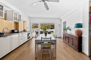 Una cocina moderna con armarios blancos, una mesa de comedor con sillas, un ventilador de techo y vistas a un patio exterior.