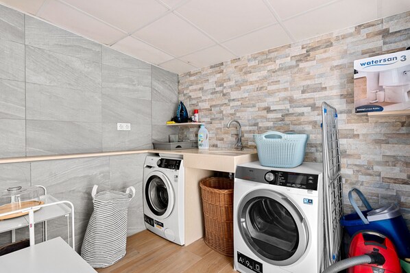 A laundry area with two washing machines, a sink, and a basket.