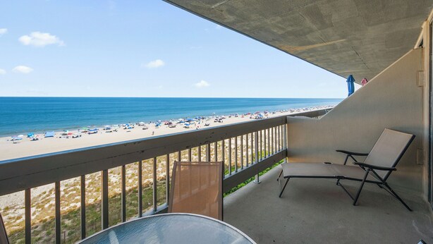 Un balcon avec vue sur la plage, une chaise longue et une table.