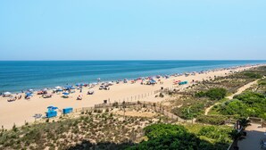Une plage dotée de nombreux parasols et de chaises longues, un sentier sablonneux et une clôture qui la sépare de la végétation.