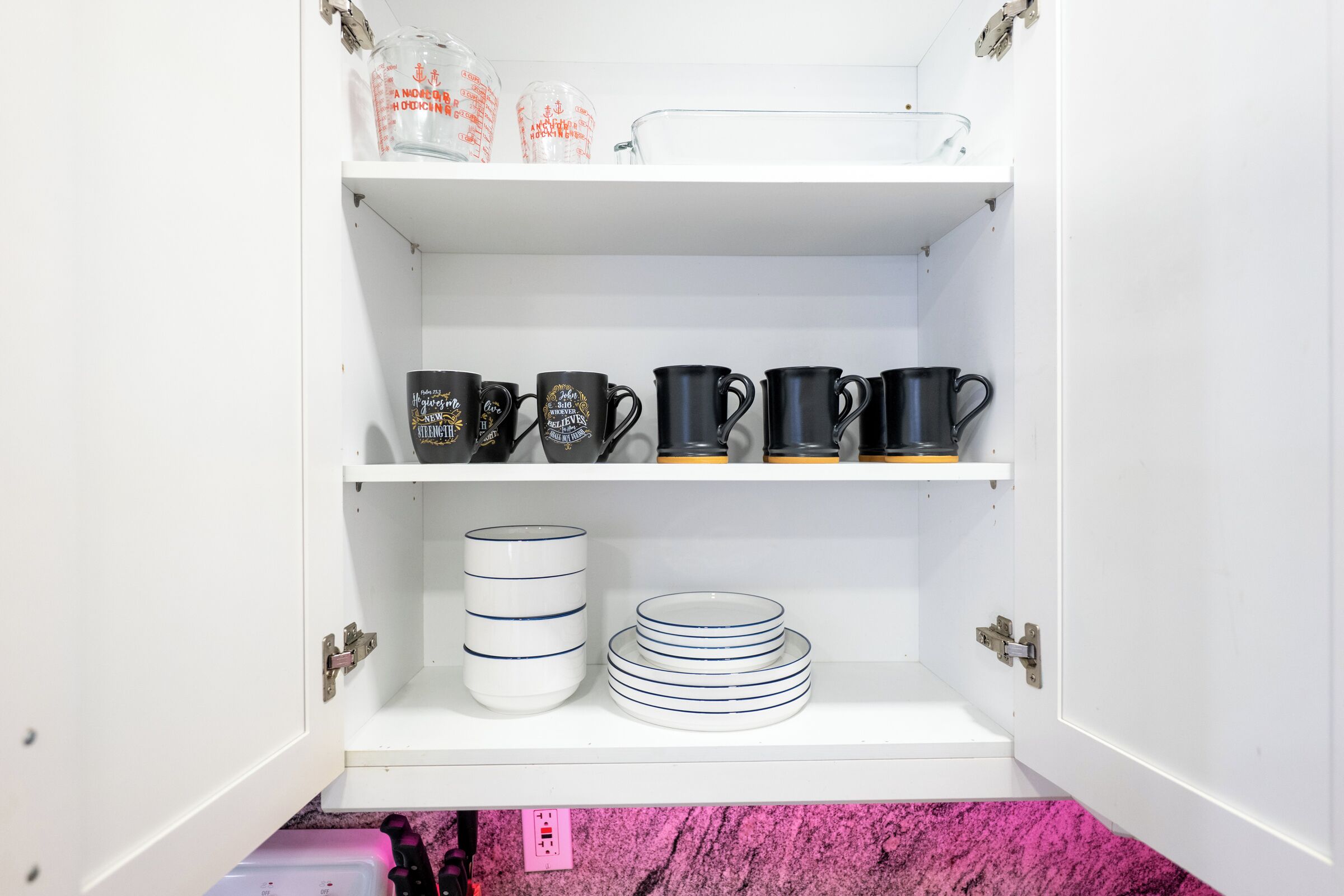 Un meuble de cuisine doté d’étagères où sont rangés divers ustensiles, notamment des tasses à mesurer, des mugs et des assiettes.