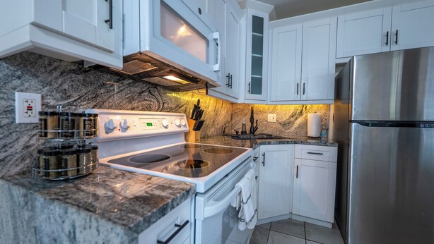 Una cocina moderna con armarios blancos, un refrigerador de acero inoxidable, horno empotrado y encimera de granito.