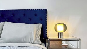 A bed with a tufted headboard, a bedside table with a lamp, and a mirror. - The Hideaway Haven (Markham)