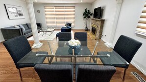 A modern living room with a glass-top dining table surrounded by four chairs, a sofa, a coffee table, and a fireplace. - The Hideaway Haven (Markham)