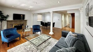 A spacious living room with a fireplace, a glass coffee table, a sofa, and a dining area with chairs. - The Hideaway Haven (Markham)