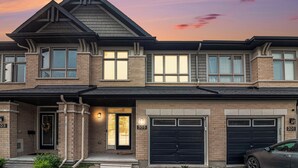 Une maison à deux étages avec une façade en briques, deux portes de garage et un porche d’entrée doté d’une porte et d’un luminaire.