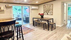 Un coin repas avec une table en bois, des chaises et un tapis. Une porte-fenêtre coulissante donne sur un patio extérieur offrant une vue sur la verdure et un drapeau américain.