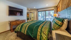 Une chambre avec un grand lit, un bureau en bois, un téléviseur à écran plat et une vue sur les arbres par la fenêtre.