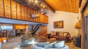Un vaste espace de vie doté d’un haut plafond, de poutres apparentes, d’un escalier, d’une cheminée et d’un coin salon confortable.