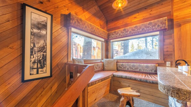 L’intérieur chaleureux d’un chalet avec des murs en bois, un banc avec des coussins, une petite table et un tableau encadré accroché au mur.