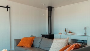 Un salon moderne avec un canapé d’angle gris, une petite table basse en bois, un lampadaire blanc et une cheminée noire.