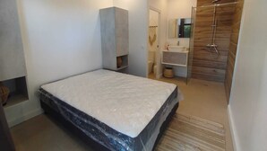 A modern bedroom with a large bed, a built-in wardrobe, a bathroom with a wooden shower enclosure, and a small sink. - An unusual haven of peace overlooking the turquoise lagoon of Haapiti in Moorea (Moorea-Maiao)