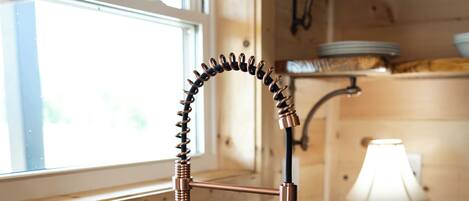 A kitchen with a copper faucet, wooden countertop, and a window.