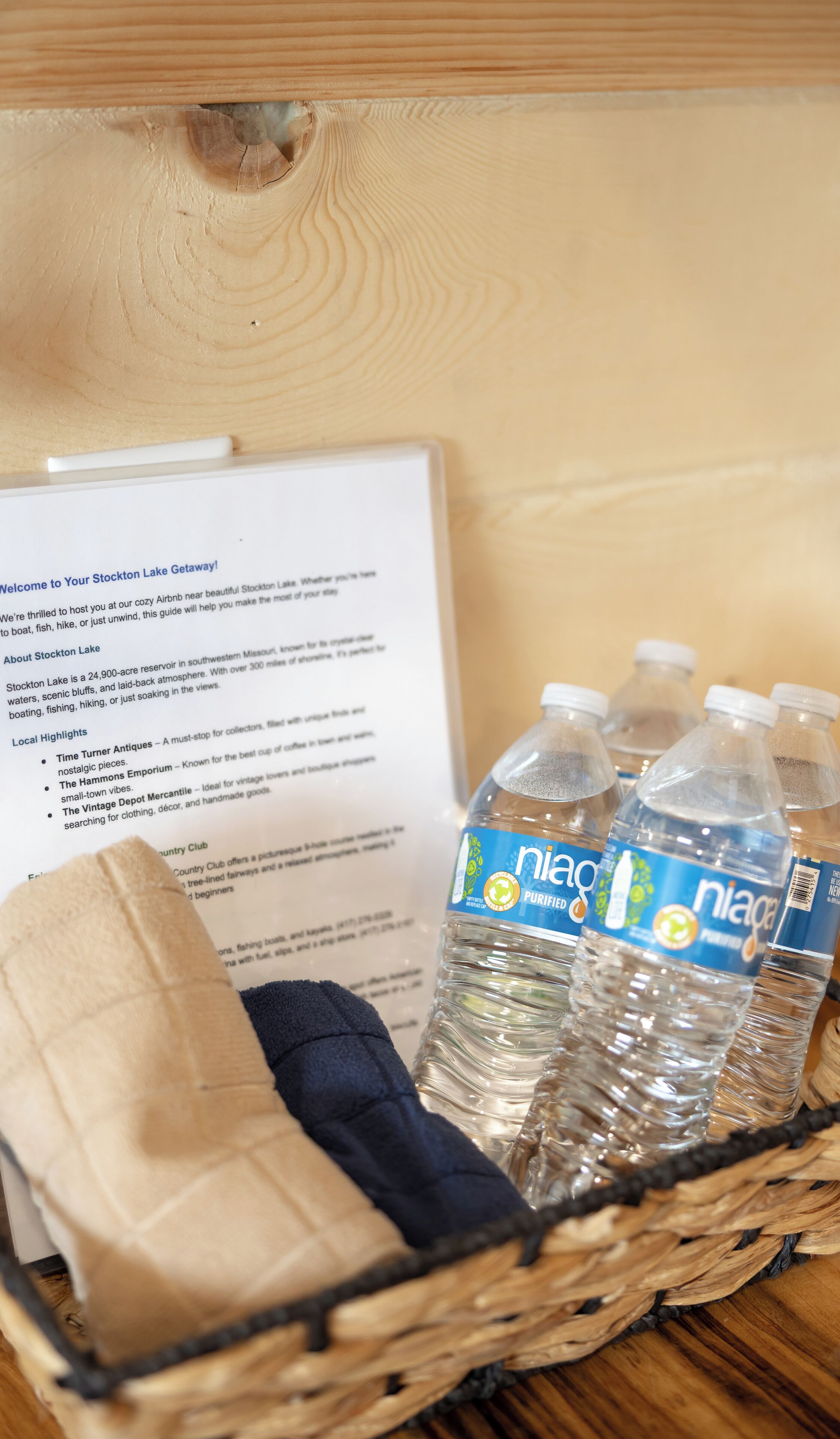 A wooden box containing a welcome guide, a pair of slippers, and several water bottles.