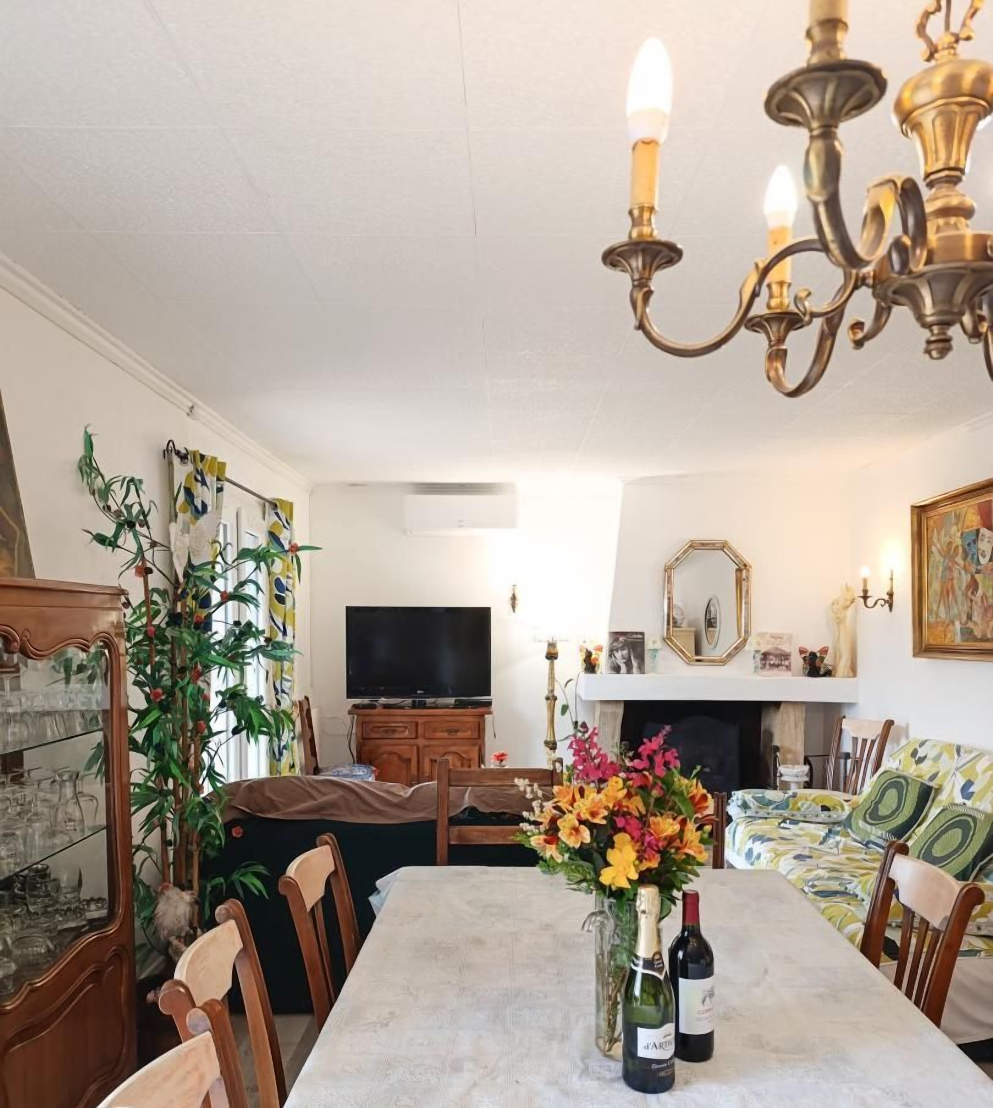 Comedor con una mesa larga, sillas, una lámpara de araña, televisor y chimenea.