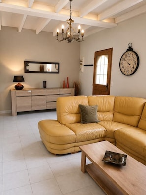 A living room with a yellow leather sofa, a wooden coffee table, a chandelier, a clock, and a sideboard.