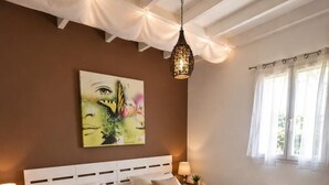 Ein Schlafzimmer mit zwei Betten, einer Hängelampe, einem Bild an der Wand und einem Fenster mit Vorhängen.