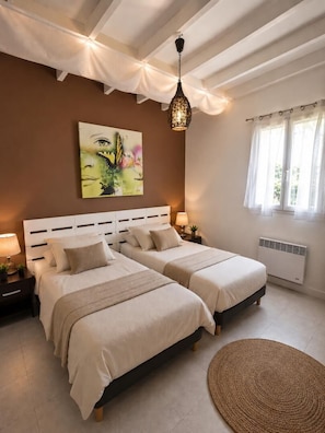 A bedroom with two beds, a hanging light fixture, a painting on the wall, and a window with curtains.