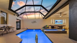 Une piscine dotée d’un toit en verre, d’un écran de télévision et d’un espace détente avec une table et des chaises.