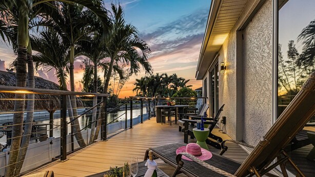Une terrasse en bois avec des sièges d’extérieur, une table avec une bouteille et des verres, et une balustrade donnant sur une étendue d’eau.