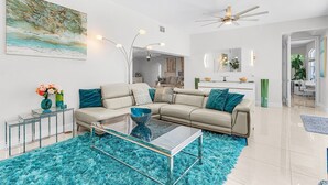 A modern living room with a sectional sofa, a glass coffee table, and a large abstract painting on the wall. - Heated Pool & Spa with Dock, Tiki Hut & Gulf Access - Coral Reef - Roelens (Cape Coral)