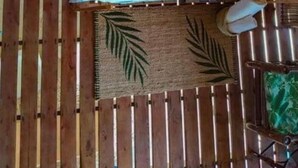Ein Bett mit grünen Kissen, einer gewebten Matte und Holzboden.