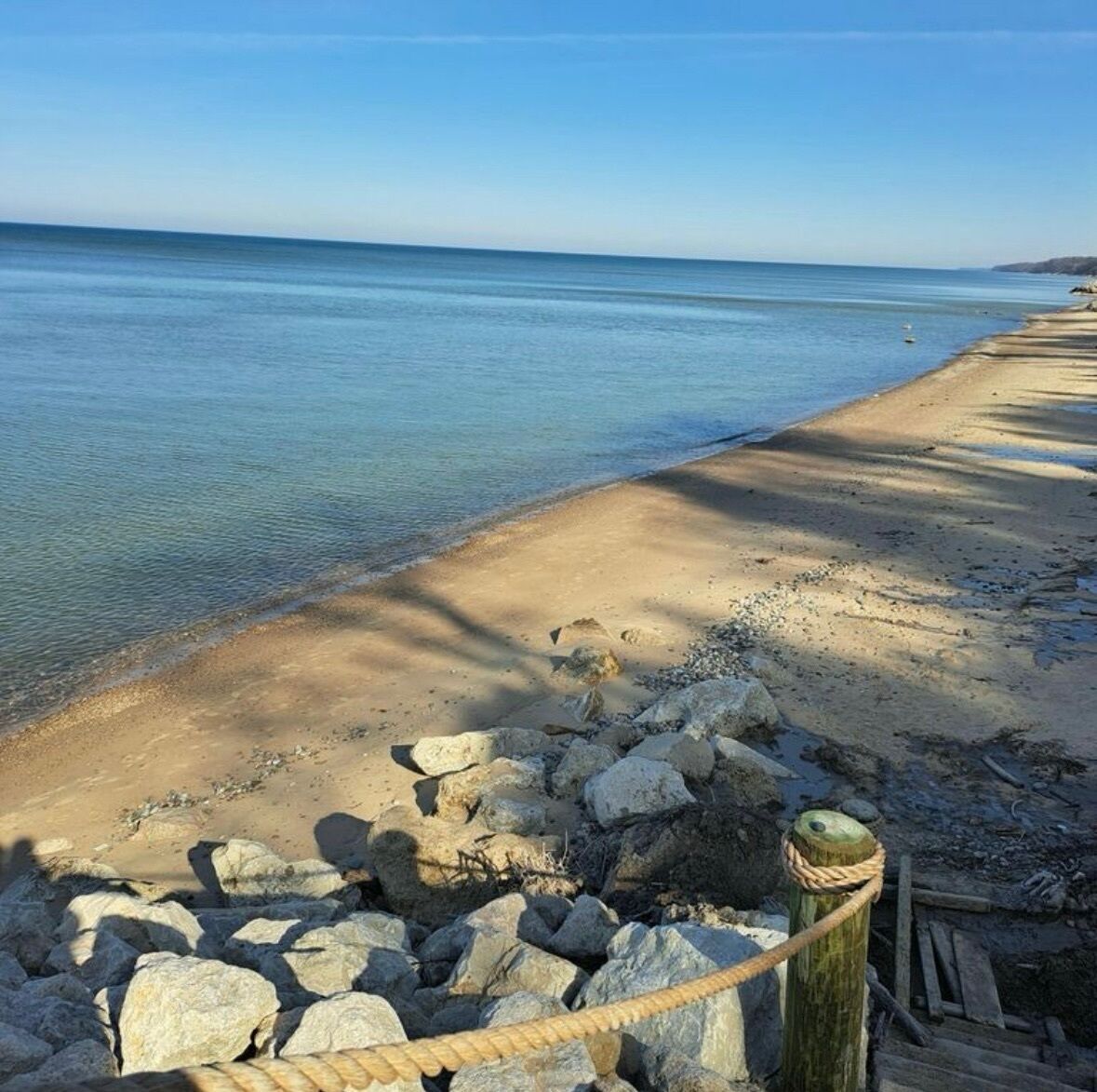 Une plage à l’eau claire, avec un rivage sablonneux et un poteau en bois muni d’une corde.