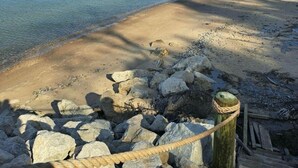 Une plage à l’eau claire, avec un rivage sablonneux et un poteau en bois muni d’une corde.