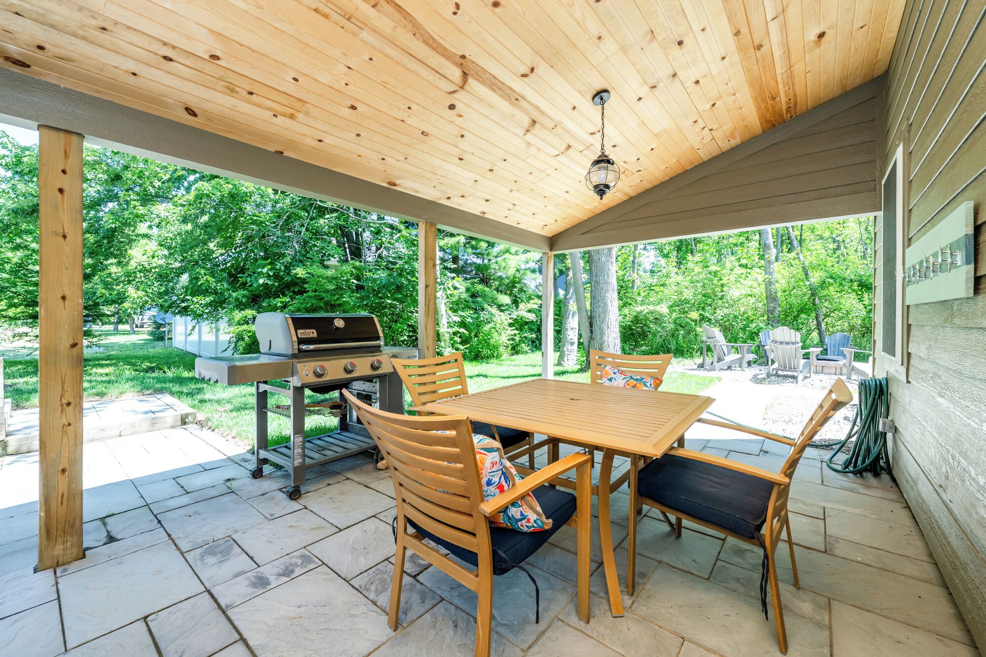 A covered patio with a wooden ceiling, a grill, and a table with chairs.