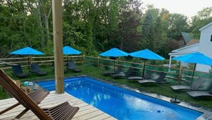 Une terrasse en bois avec une piscine, des chaises longues et des parasols.