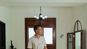 Een man staat in een kamer met een kamer met een patroon vloer, een houten deur en een kroonluchter.