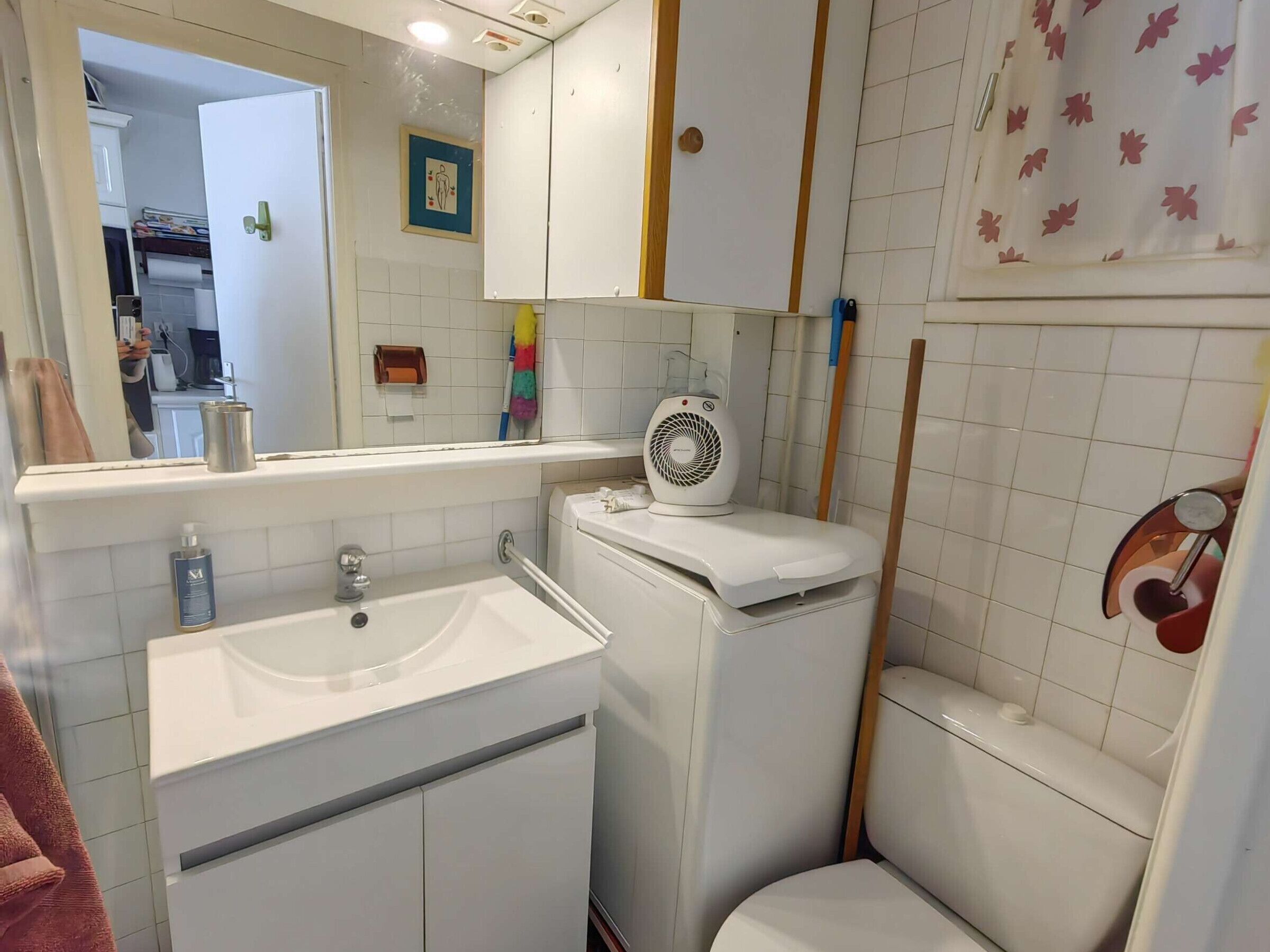 A bathroom with a white sink, toilet, and a mirror. There is a fan on the toilet and a towel rack on the wall.