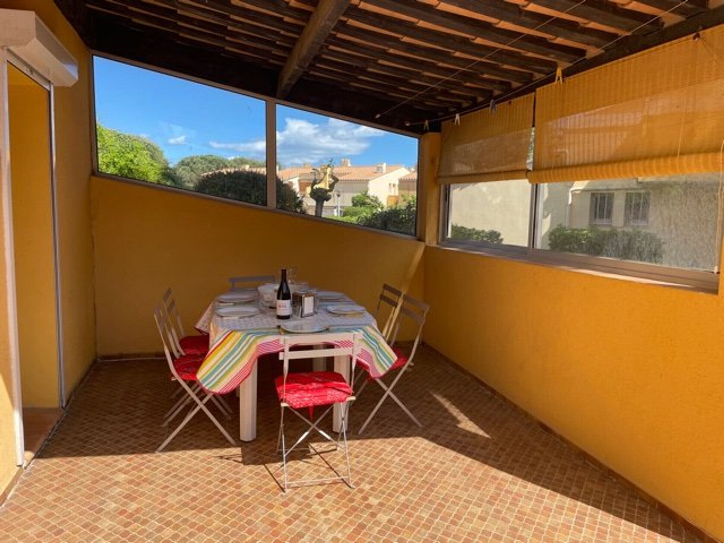 Um alpendre coberto com uma mesa posta para dois, uma garrafa de vinho e cadeiras confortáveis acolchoadas em vermelho.
