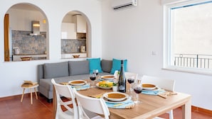 A dining area with a wooden table set for four, a sofa with teal cushions, and a kitchen visible through an archway. - Casa Serafina - Sinfonia (Letojanni)