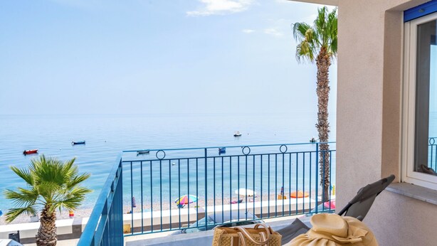 A balcony with a view of the sea, a palm tree, and a beach with umbrellas. - Casa Serafina - Sinfonia (Letojanni)