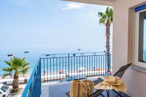Un balcon avec vue sur la mer, un palmier et une plage parsemée de parasols.