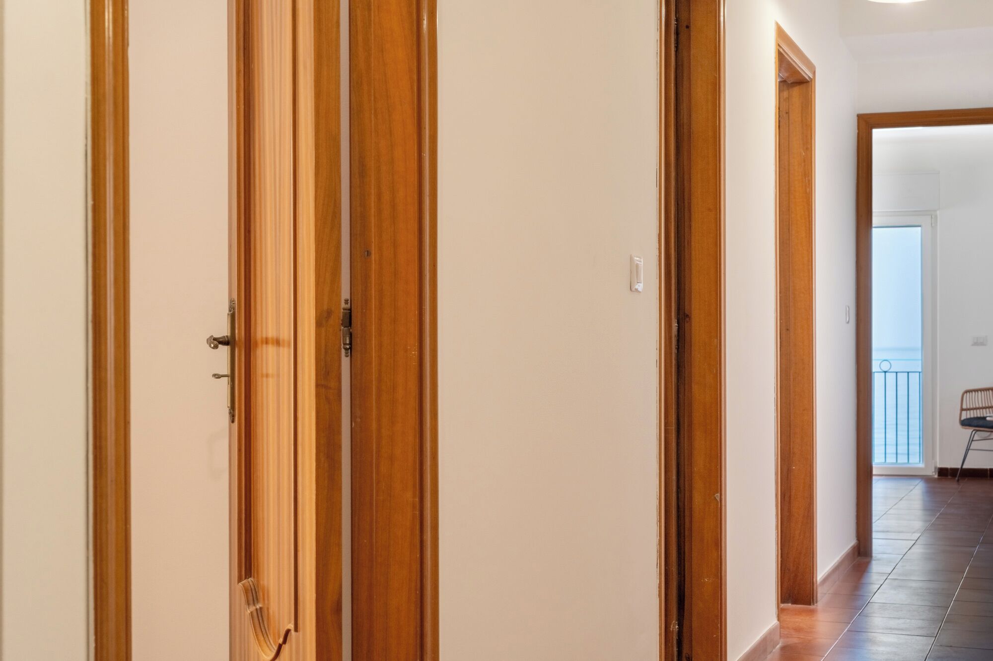 A hallway with wooden doors and a view into a room with a balcony.