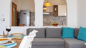 A modern living room with a grey sofa, teal cushions, and a dining area with plates and a glass of red wine. - Casa Serafina - Sinfonia (Letojanni)