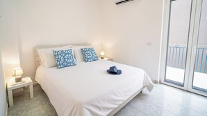 Un dormitorio con una cama, dos almohadas estampadas, un control remoto, una lámpara y un equipo de aire acondicionado.