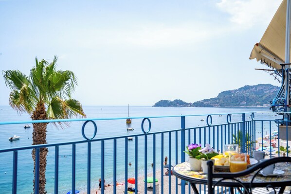 Un balcon avec vue sur la mer, un palmier et une table avec des boissons et des fleurs.