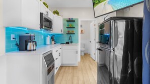 A modern kitchen with white cabinets, a black refrigerator, a coffee maker, and a teal backsplash. - Beautiful 3/3 Island Retreat with Heated Pool, Dock & Private Boat Ramp. (Bokeelia)