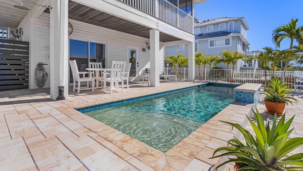 A pool area with a clear blue pool, white outdoor furniture, and a white building with a balcony. - Beautiful 3/3 Island Retreat with Heated Pool, Dock & Private Boat Ramp. (Bokeelia)