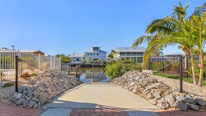 A pathway leading to a body of water with houses in the background. - Beautiful 3/3 Island Retreat with Heated Pool, Dock & Private Boat Ramp. (Bokeelia)