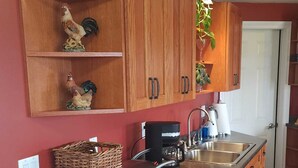 Une cuisine avec des meubles en bois, un évier en acier inoxydable, une machine à café et une statuette de coq décorative.