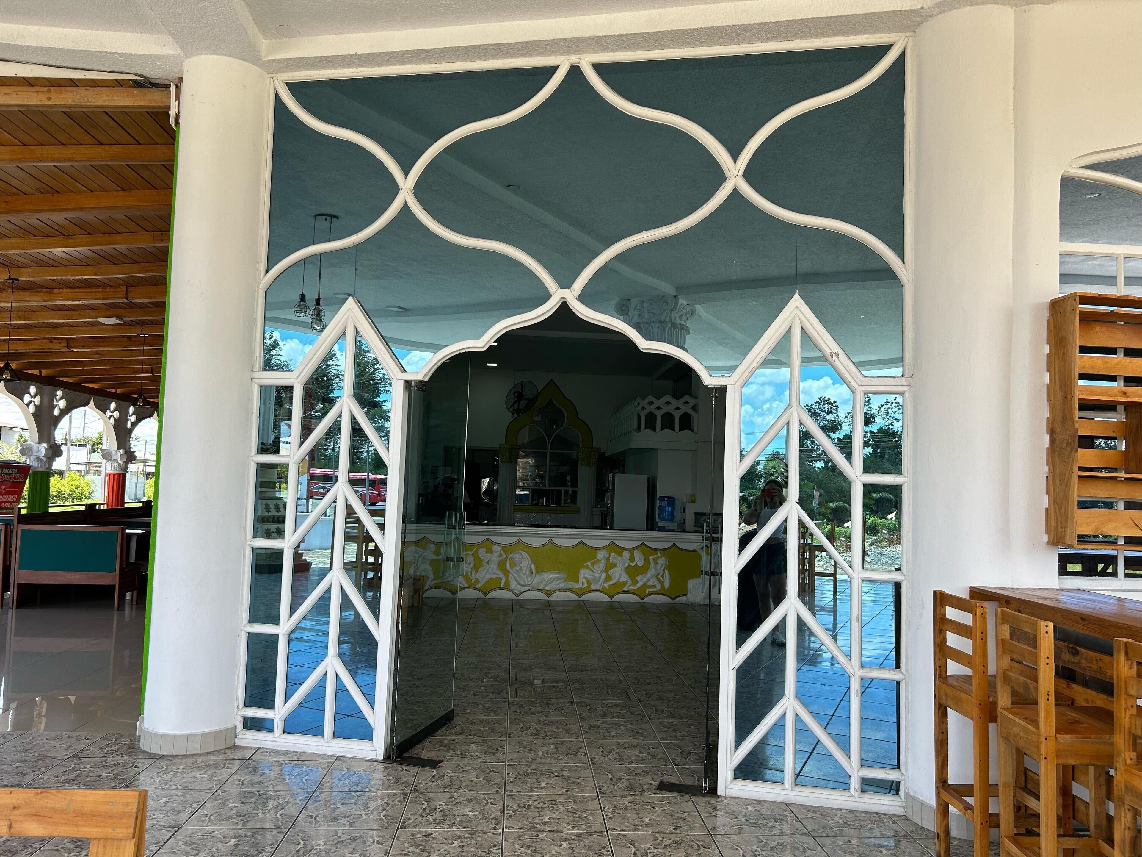 Un ristorante con pavimento piastrellato, un bancone con schienale a mosaico giallo e bianco e vista sull'esterno attraverso un'ampia finestra.