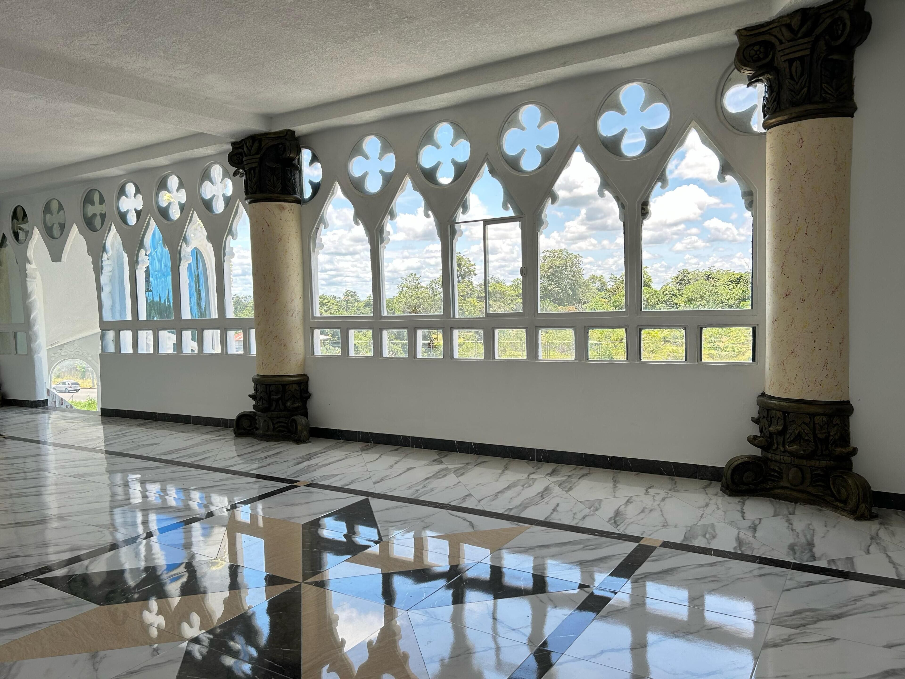 A spacious hall with marble flooring, large arched windows, and decorative columns.